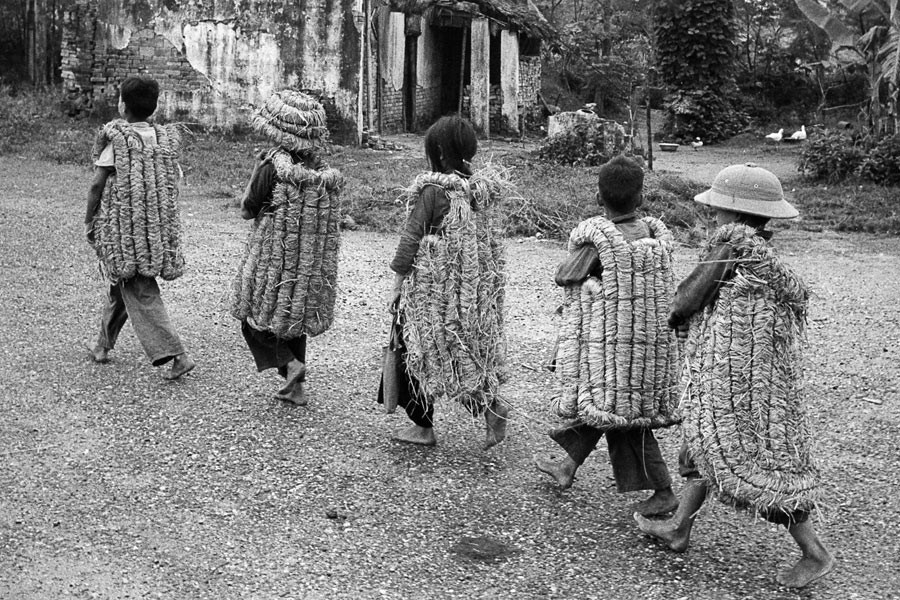 Enfants allant à l'école, portant des "armures" de paille censées les protéger des éclats de bombes. Nord Vietnam, 1969